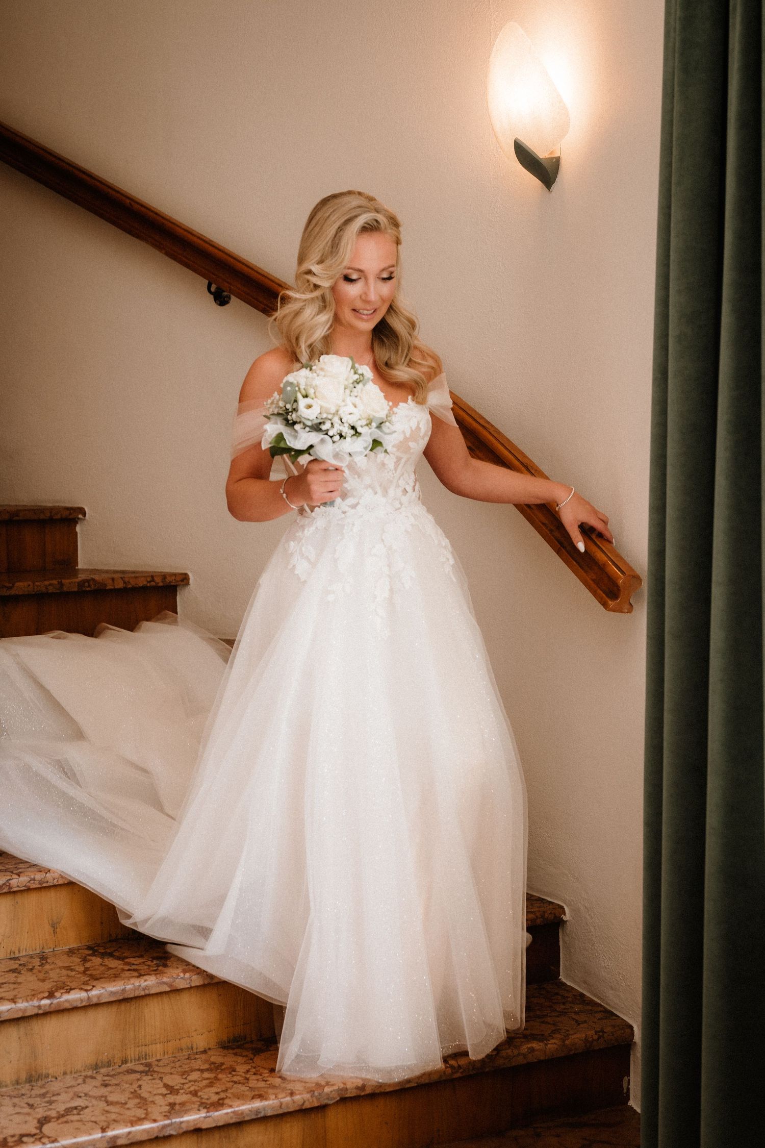 Elegant bridal moment captured on wooden stairs with flowing white tulle gown.
