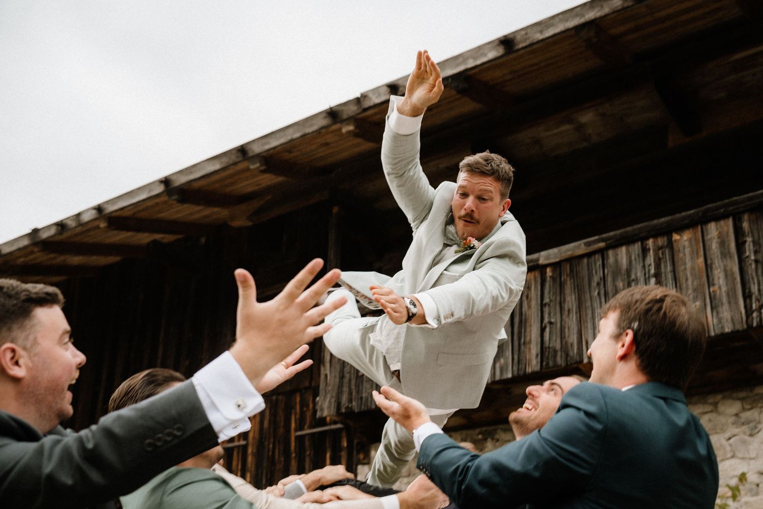 Groomsmen jumping and celebrating with high energy against rustic barn backdrop.