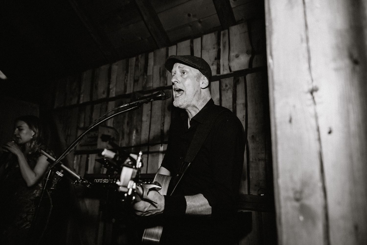 Black and white photo of musicians performing at a rustic venue.