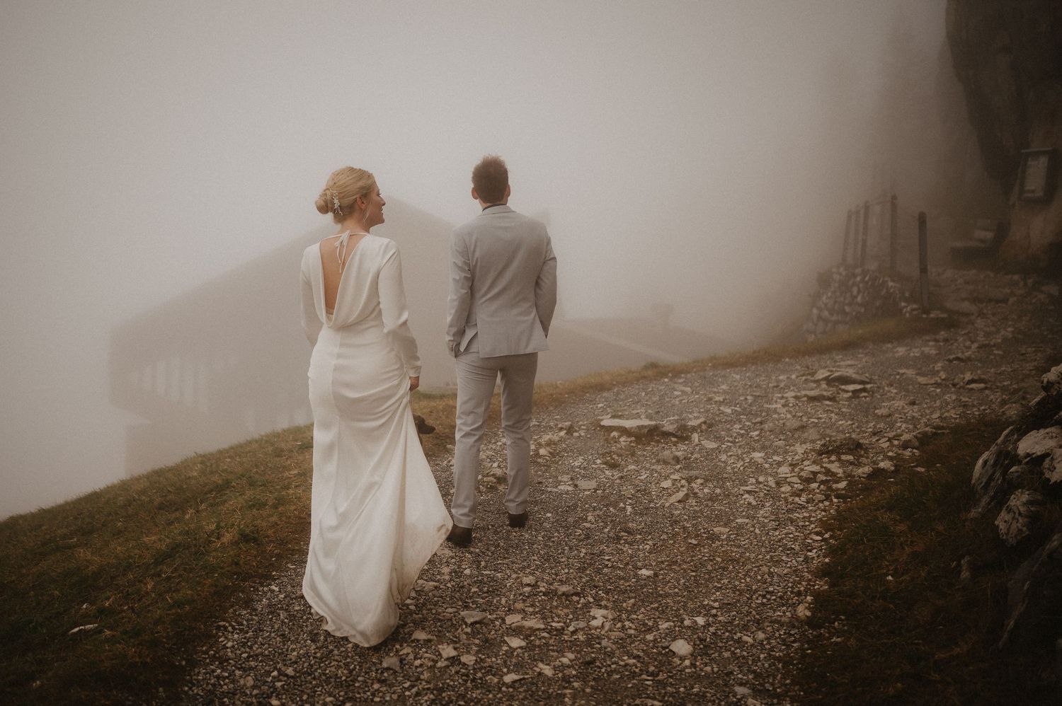 Two people walk hand in hand along a foggy mountain path.