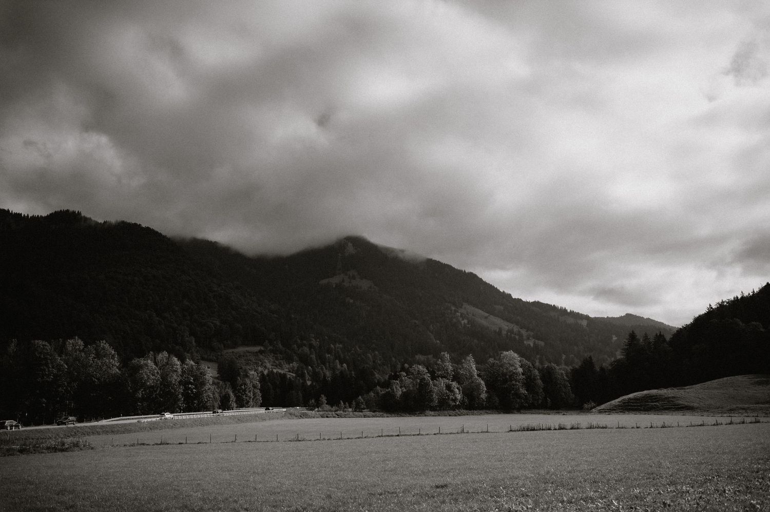Dramatic black and white landscape of mountains under stormy skies with meadow in foreground.