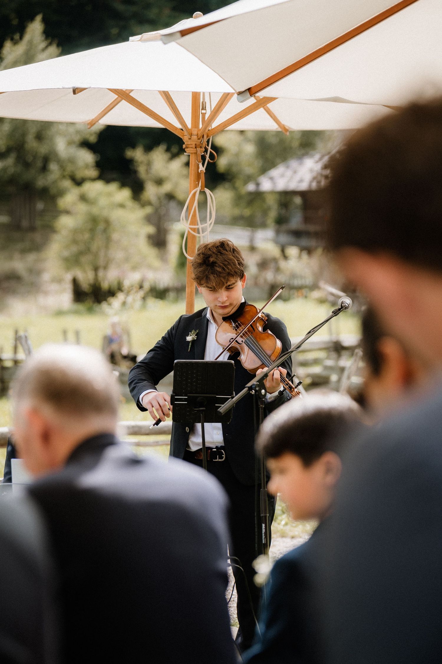 A violinist performs classical music outdoors under a white umbrella during an elegant event.