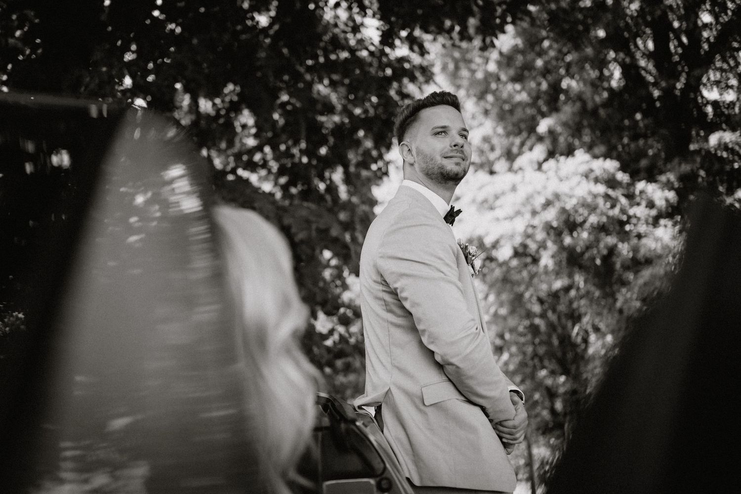Black and white artistic photo of wedding guests mingling under trees.