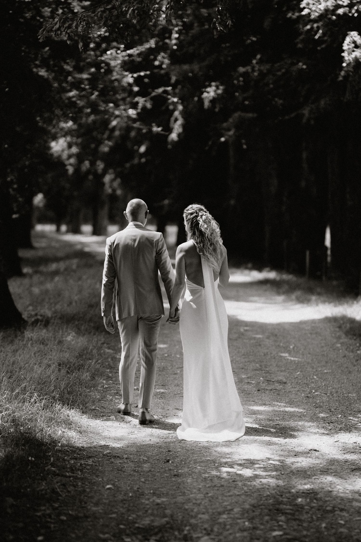 Black and white wedding photo of newlyweds walking together on a scenic woodland path.