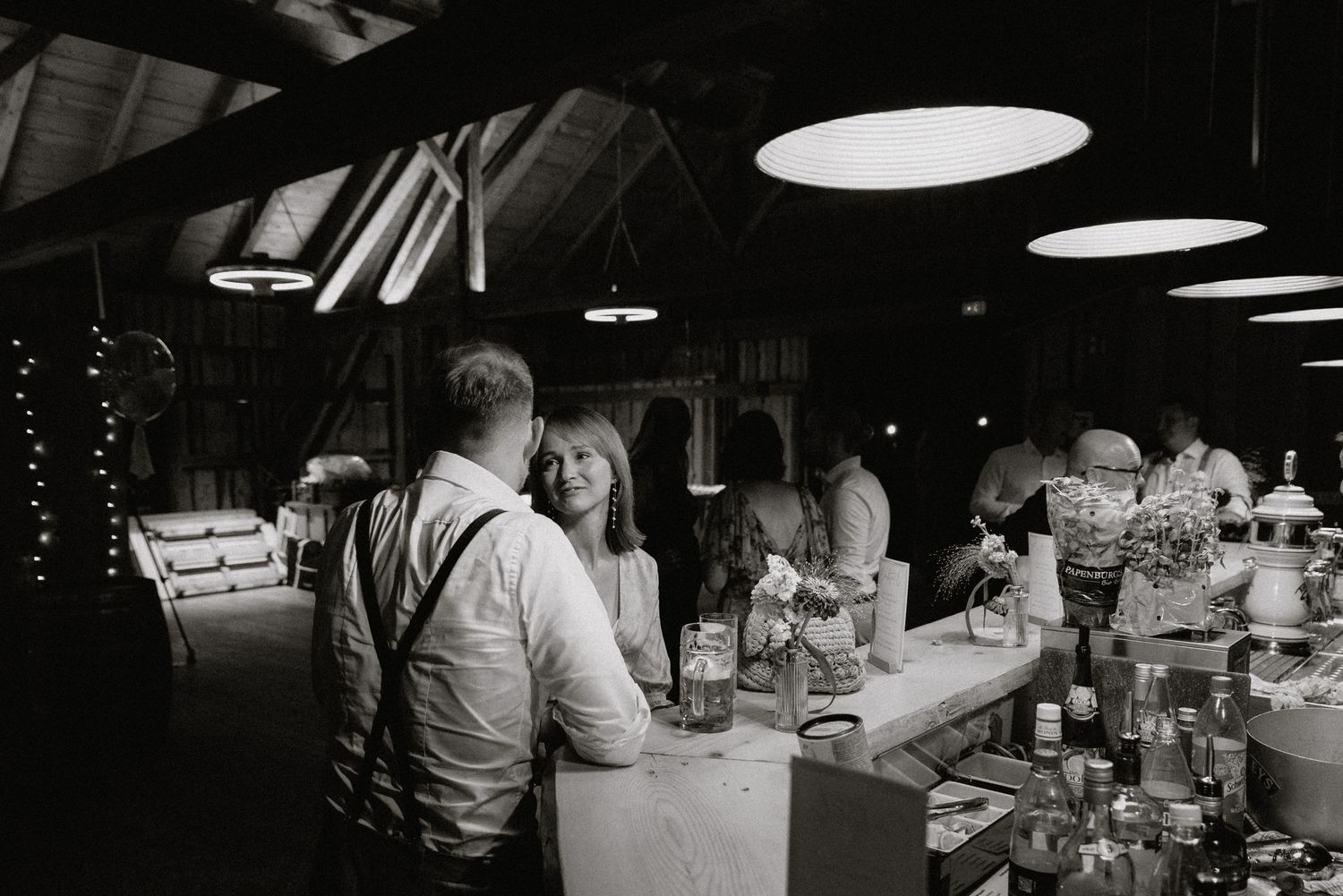 Black and white panoramic view of a wedding reception bar area with ambient lighting.