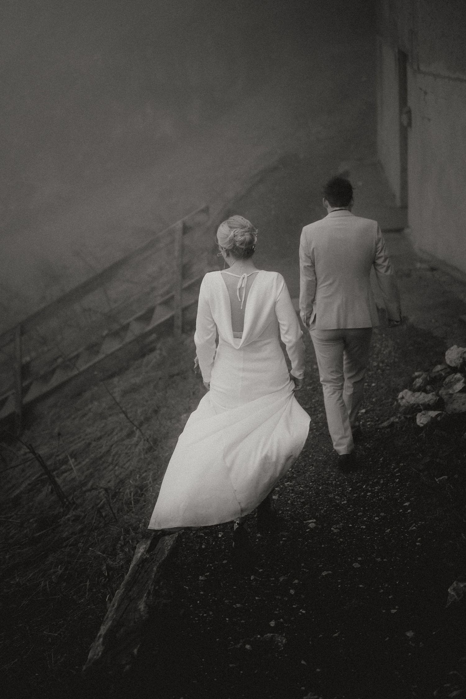 Black and white photo of a couple walking up a steep mountain slope in formal attire.