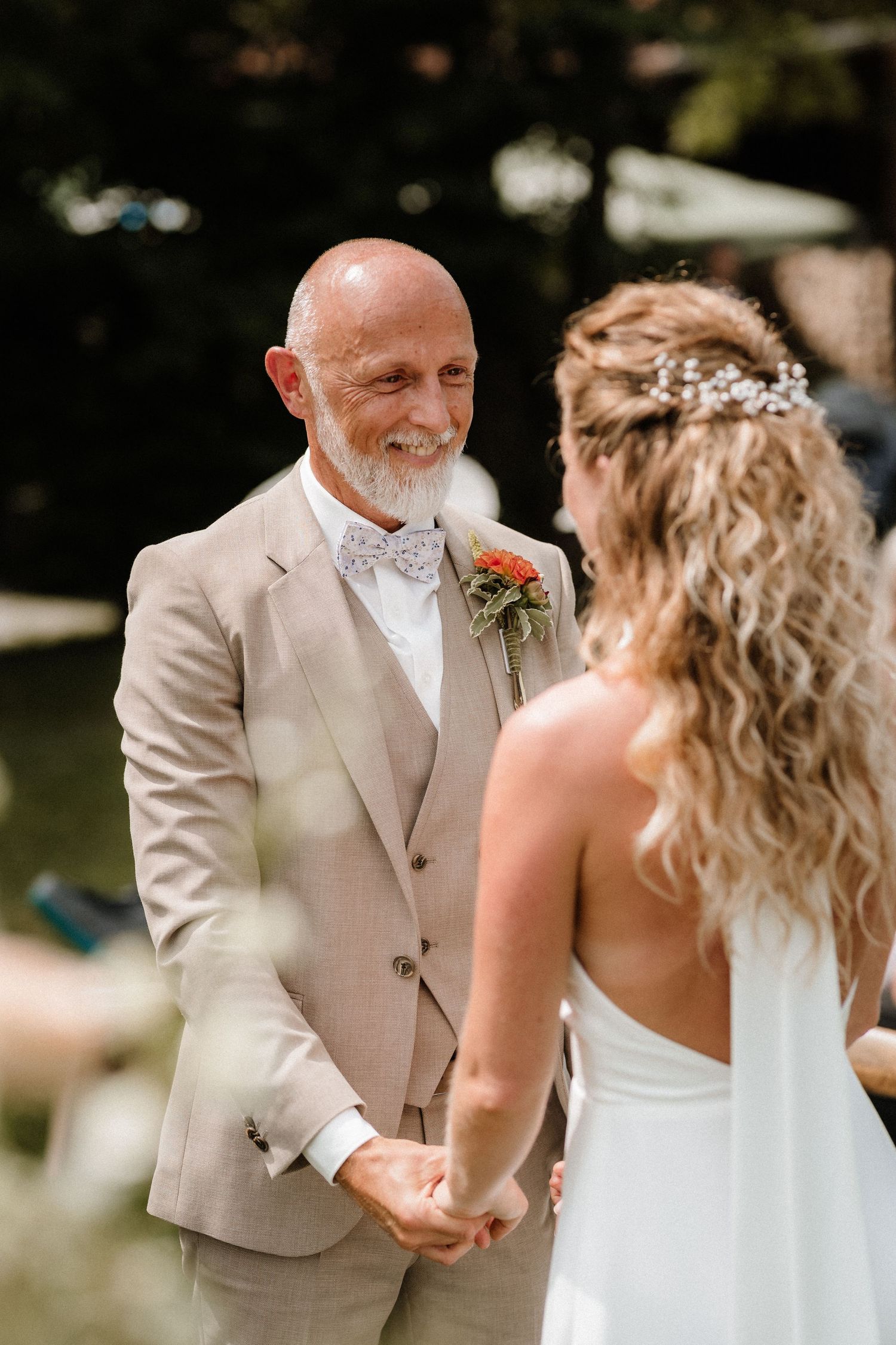 A couple shares a joyful first dance moment at an outdoor wedding reception in beige and white attire.