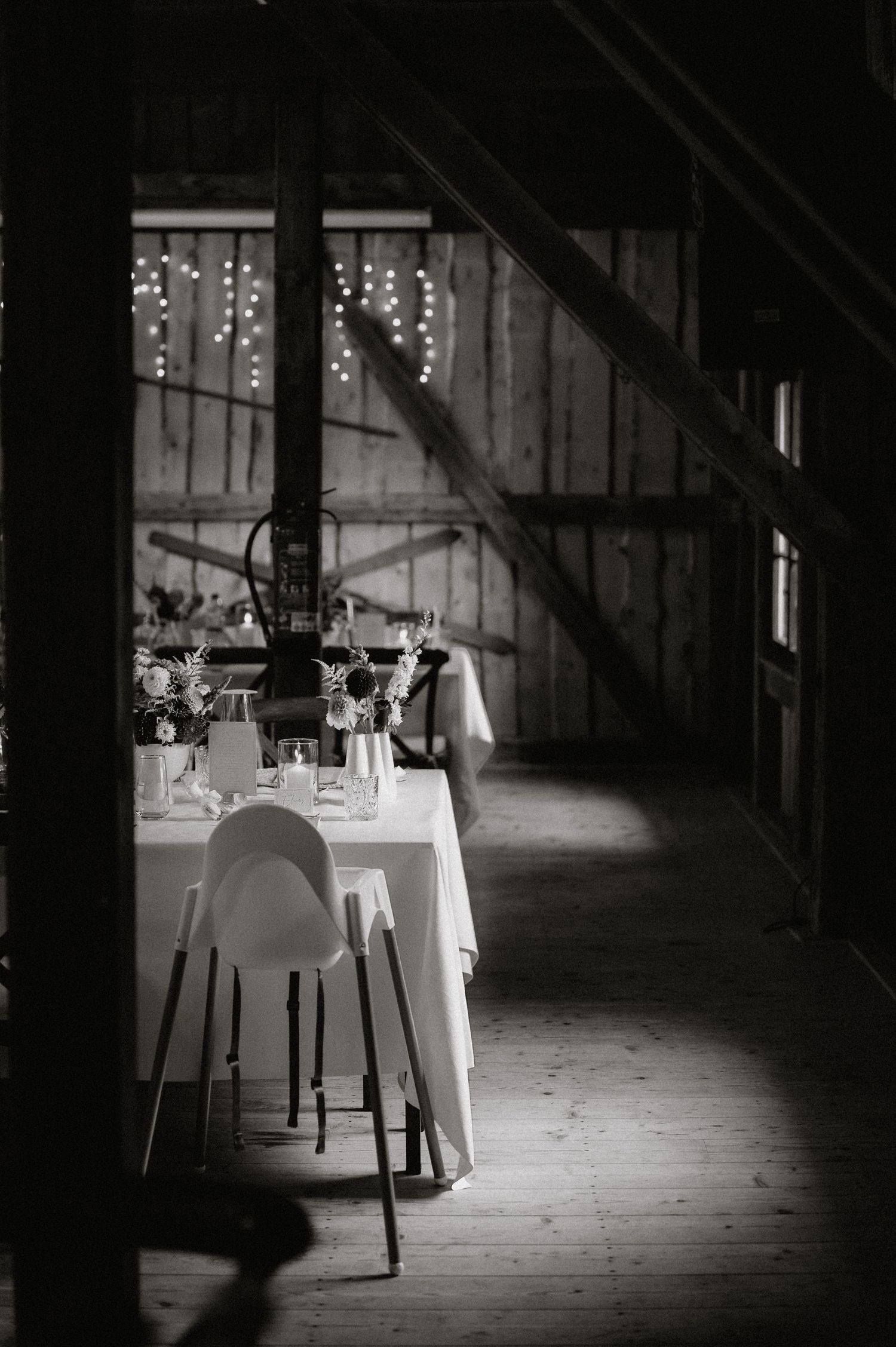 Moody lighting illuminates empty wedding reception tables in a rustic barn venue.