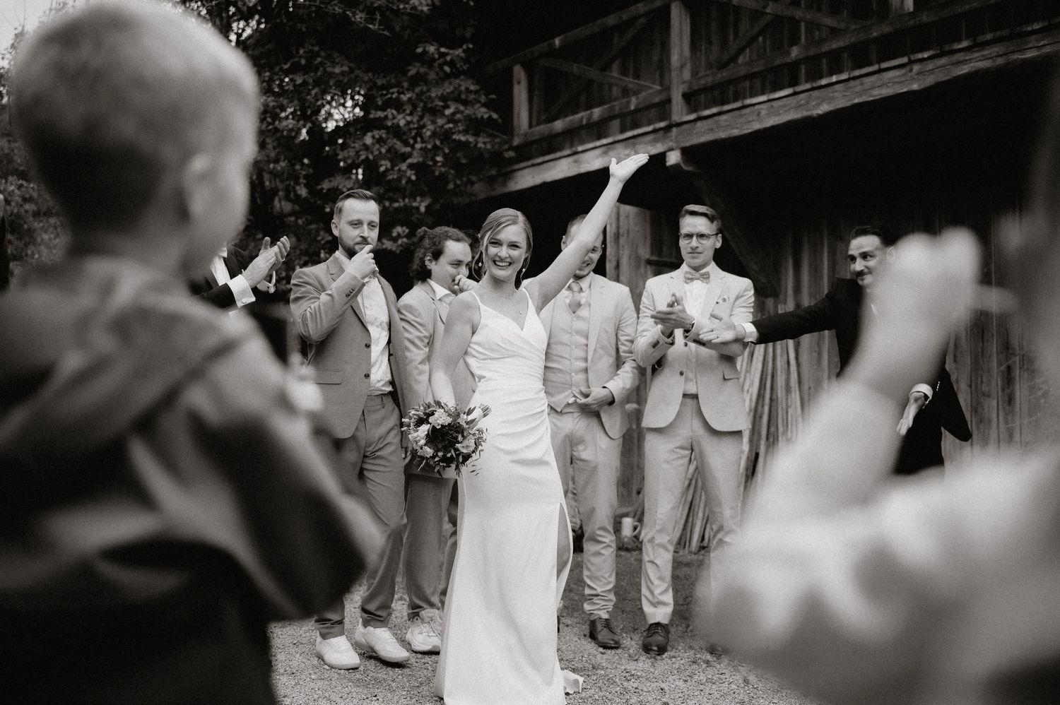 Black and white photo of wedding party members posing together near rustic barn structure.