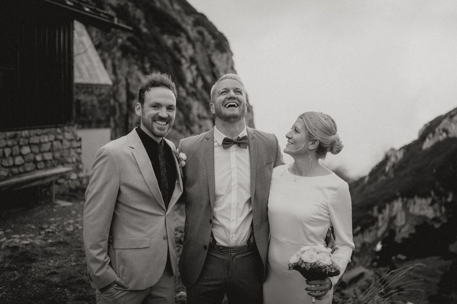A joyful wedding moment captured in black and white against a mountainous landscape.