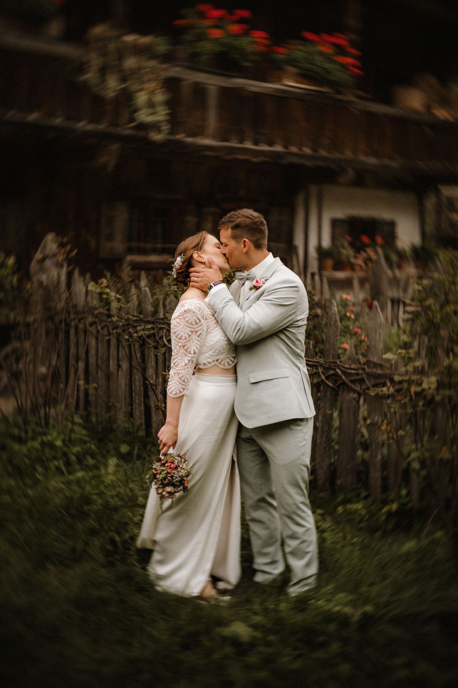 Intimate wedding moment captured in front of rustic wooden fence and garden.