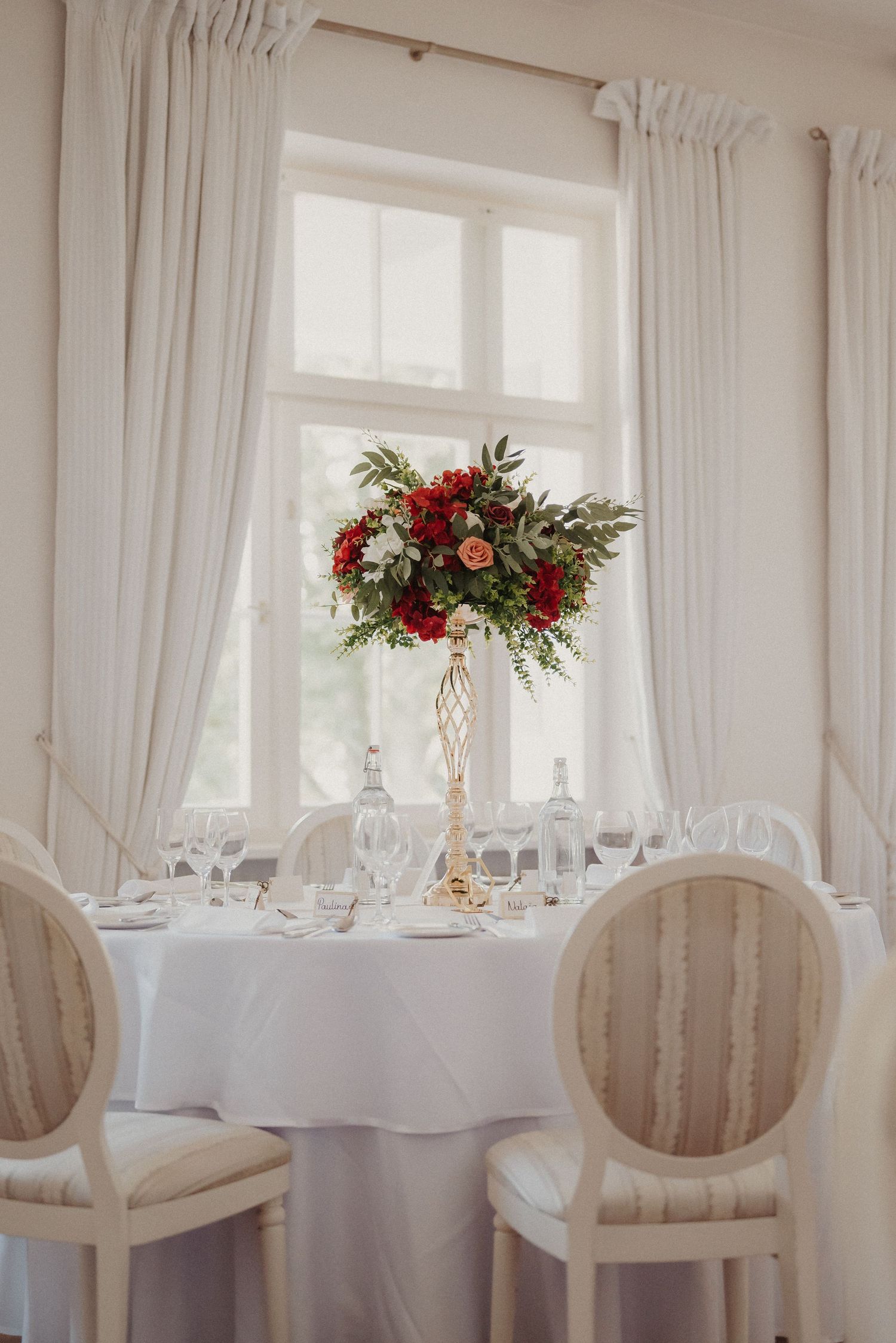 Elegant white wedding reception room with round tables, striped chairs and floral centerpieces.
