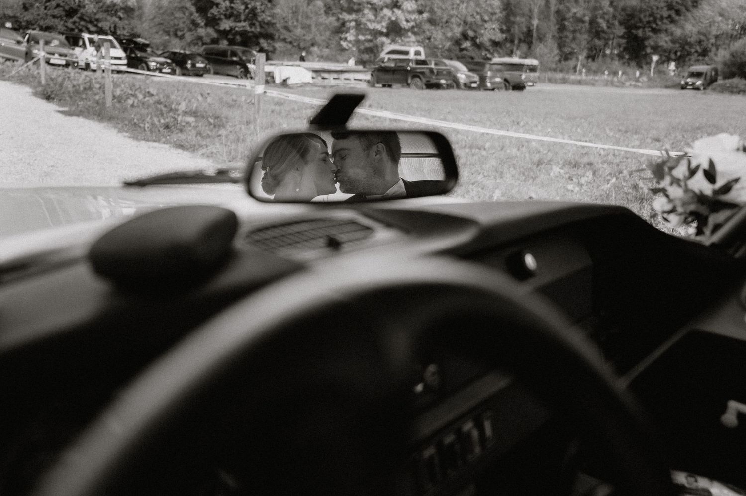 Black and white view of car rearview mirror and dashboard interior.