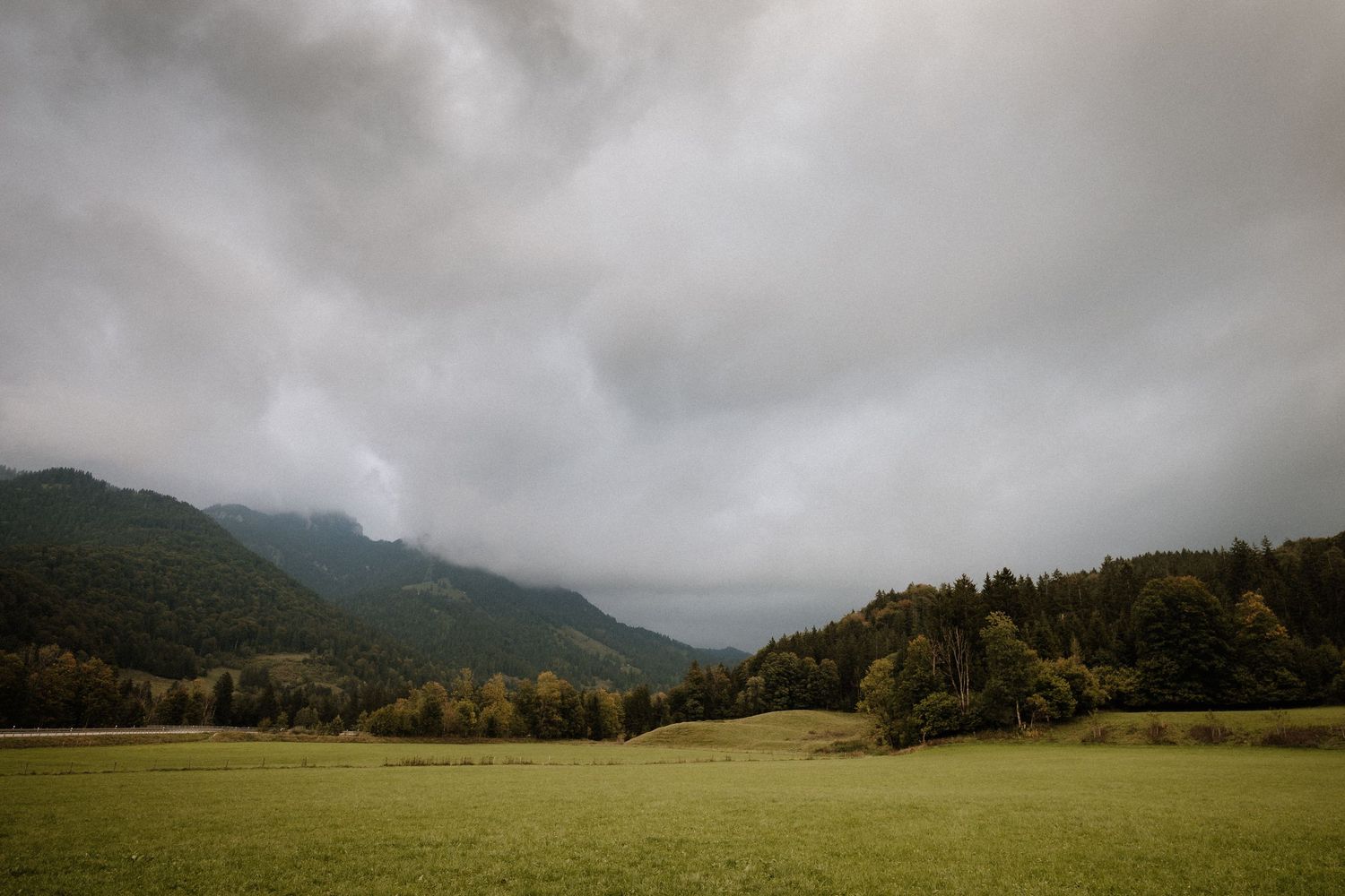 Dramatic cloudy mountain landscape with rolling hills and forest in the distance.