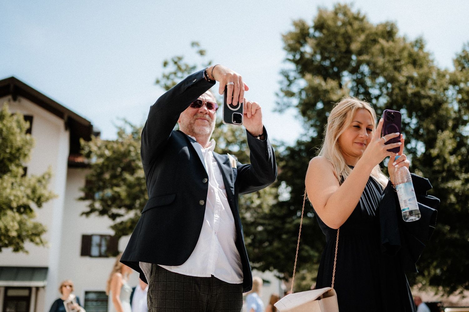 Wedding guests taking photos with smartphones at an outdoor celebration.