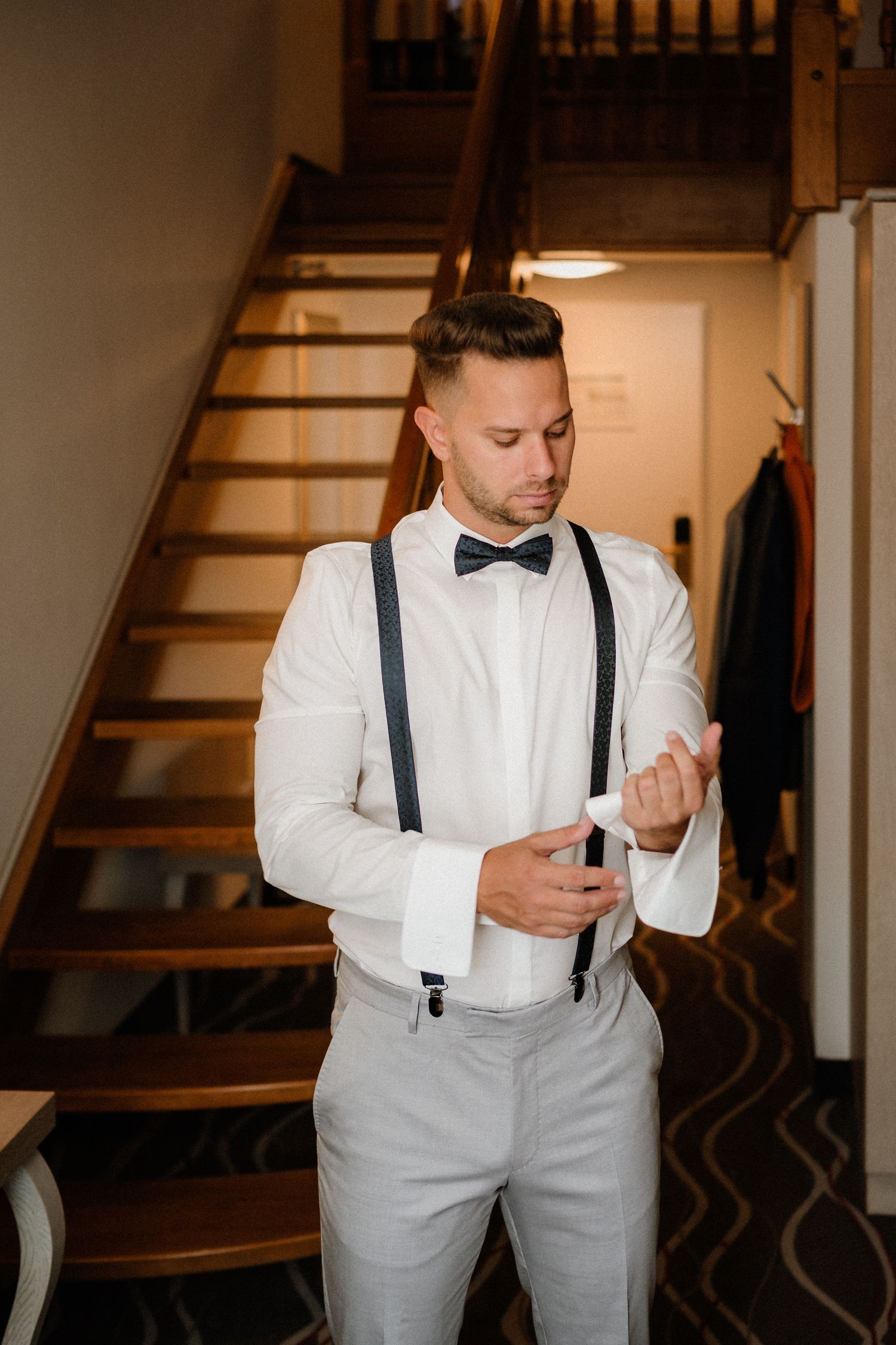 Wedding preparation scene near wooden stairs showing formal attire and bow tie.