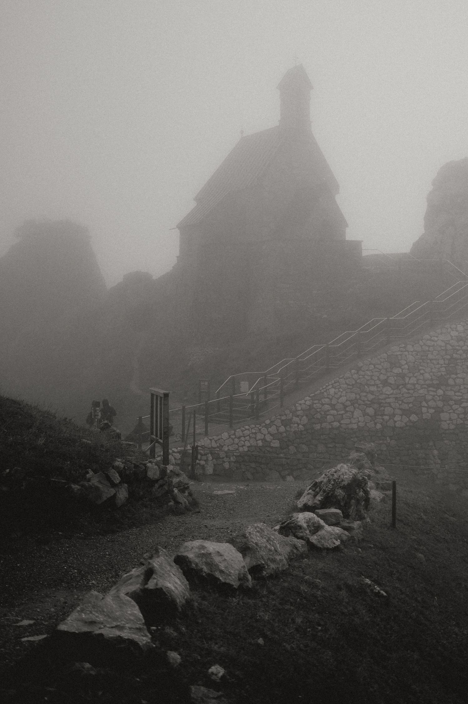 Moody black and white photograph of a church silhouette emerging from dense mountain fog.
