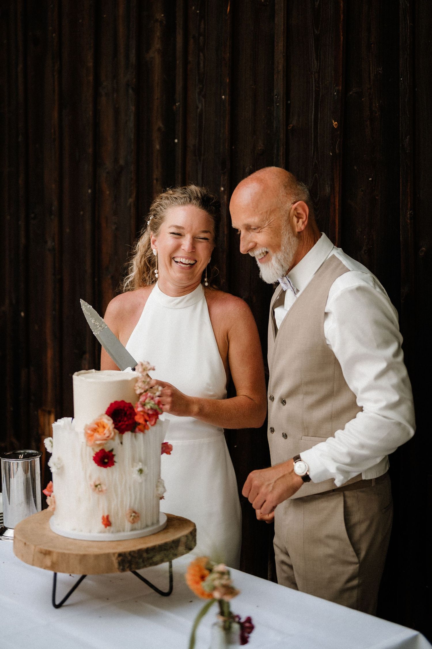 Couple cutting their white wedding cake decorated with colorful flowers.