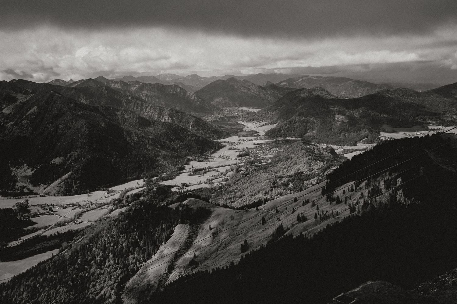 Dramatic black and white aerial view of a mountain valley with winding roads and rugged terrain.