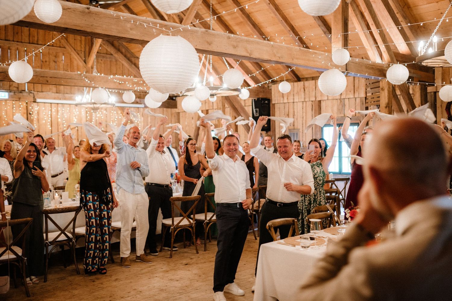Wedding guests celebrating in a barn venue with paper lanterns and warm lighting.