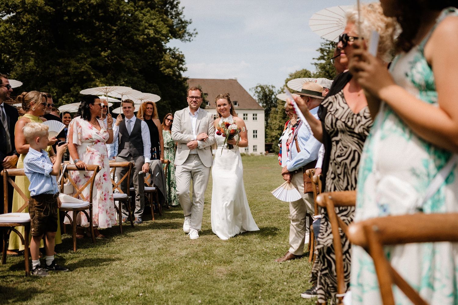 Wedding guests gather under blue skies at an outdoor summer celebration.