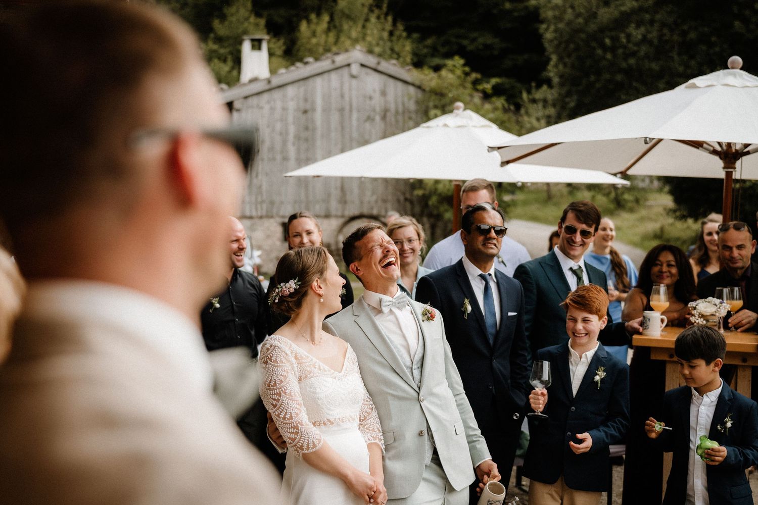 Outdoor wedding ceremony under white umbrellas with guests gathered in a garden setting.