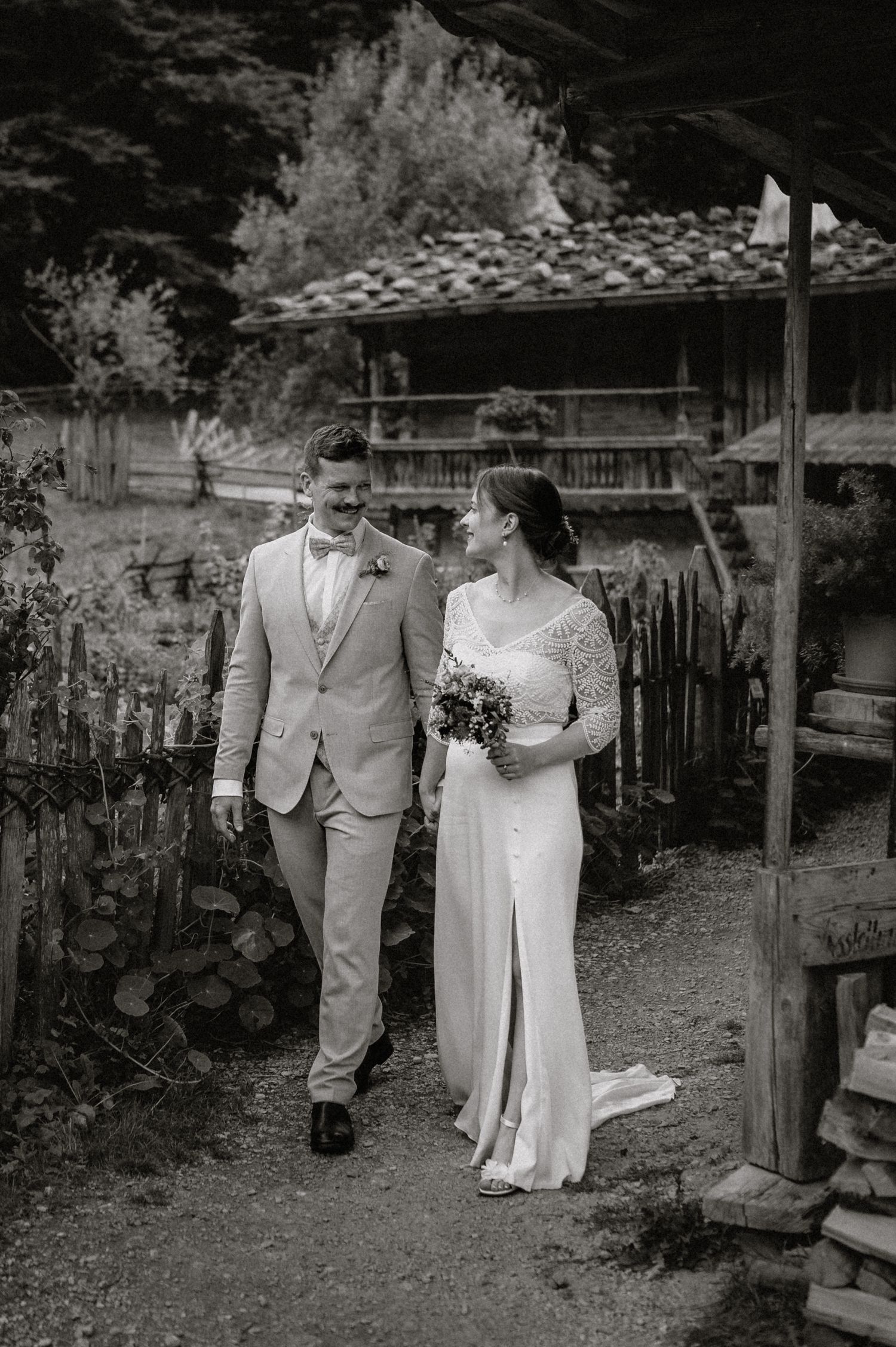 Black and white portrait of couple walking through rustic garden setting.