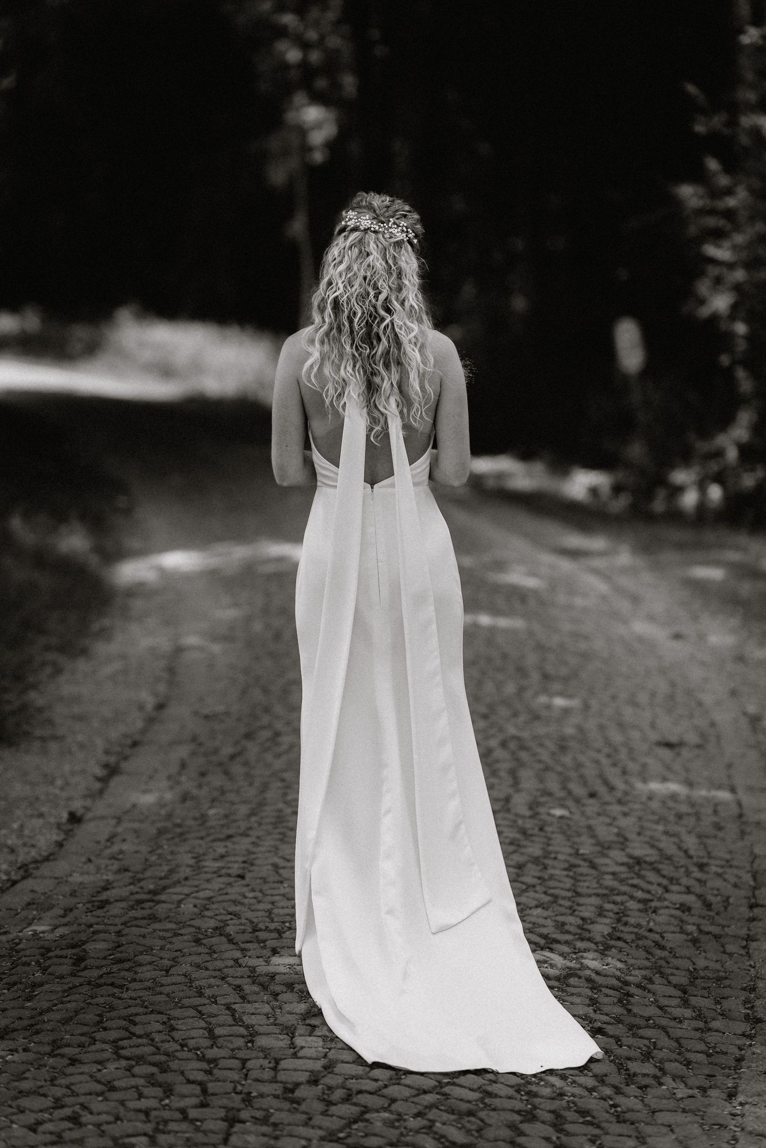 A flowing white wedding dress train trails behind on a cobblestone path.