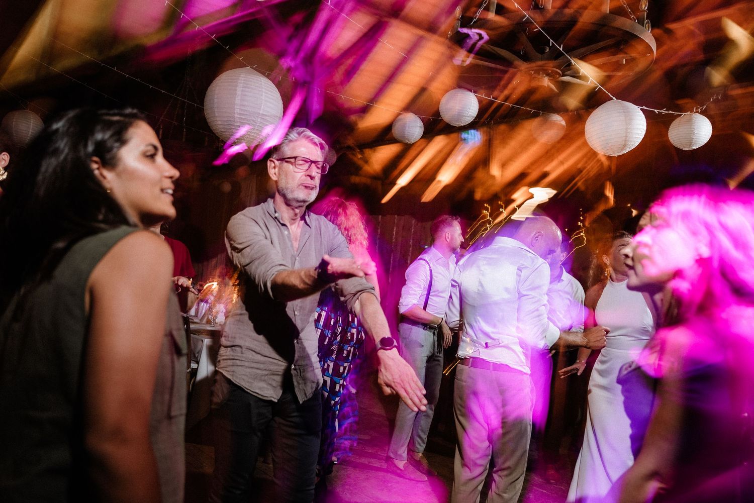 Guests celebrating at a wedding reception with dramatic pink lighting and paper lantern decorations.