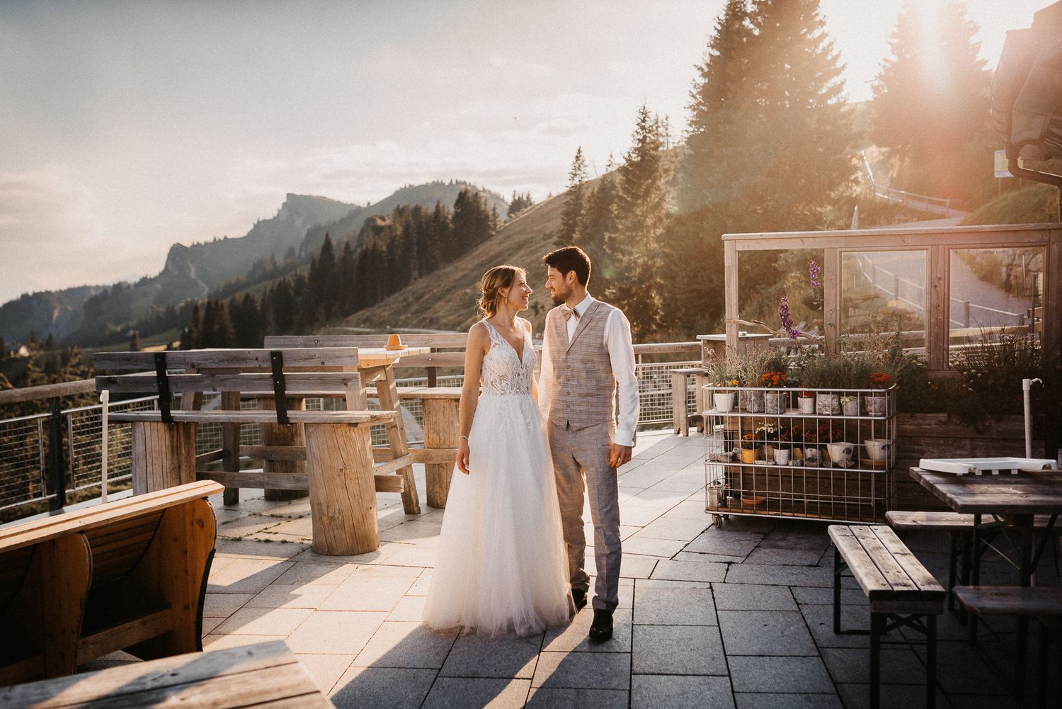 Ein Paar teilt einen intimen Moment bei Sonnenuntergang auf einer Berghütte mit malerischem Bergblick im Hintergrund. Von Dama Fotografie