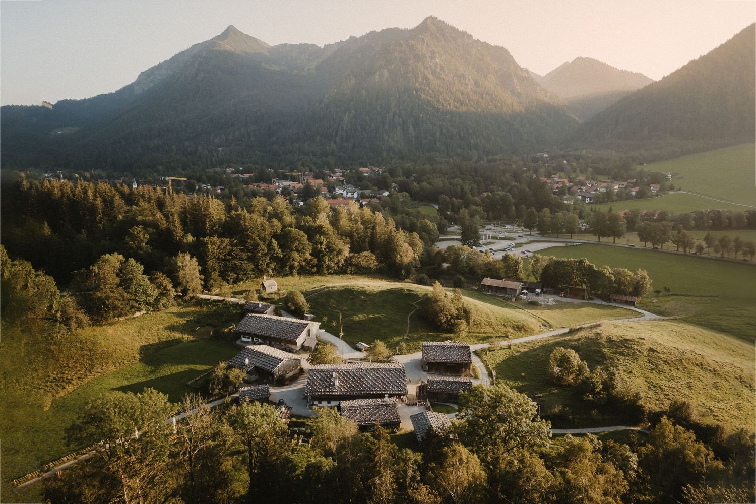 Aerial view of a luxury resort nestled in the Austrian Alps with mountains and forest during golden hour.