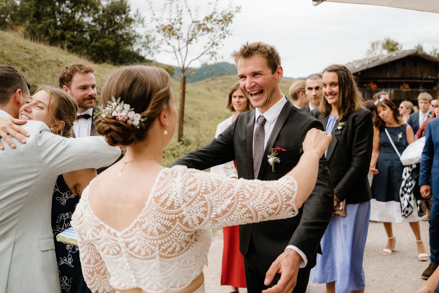 Wedding party celebrates on a gravel path with umbrellas and mountain views.