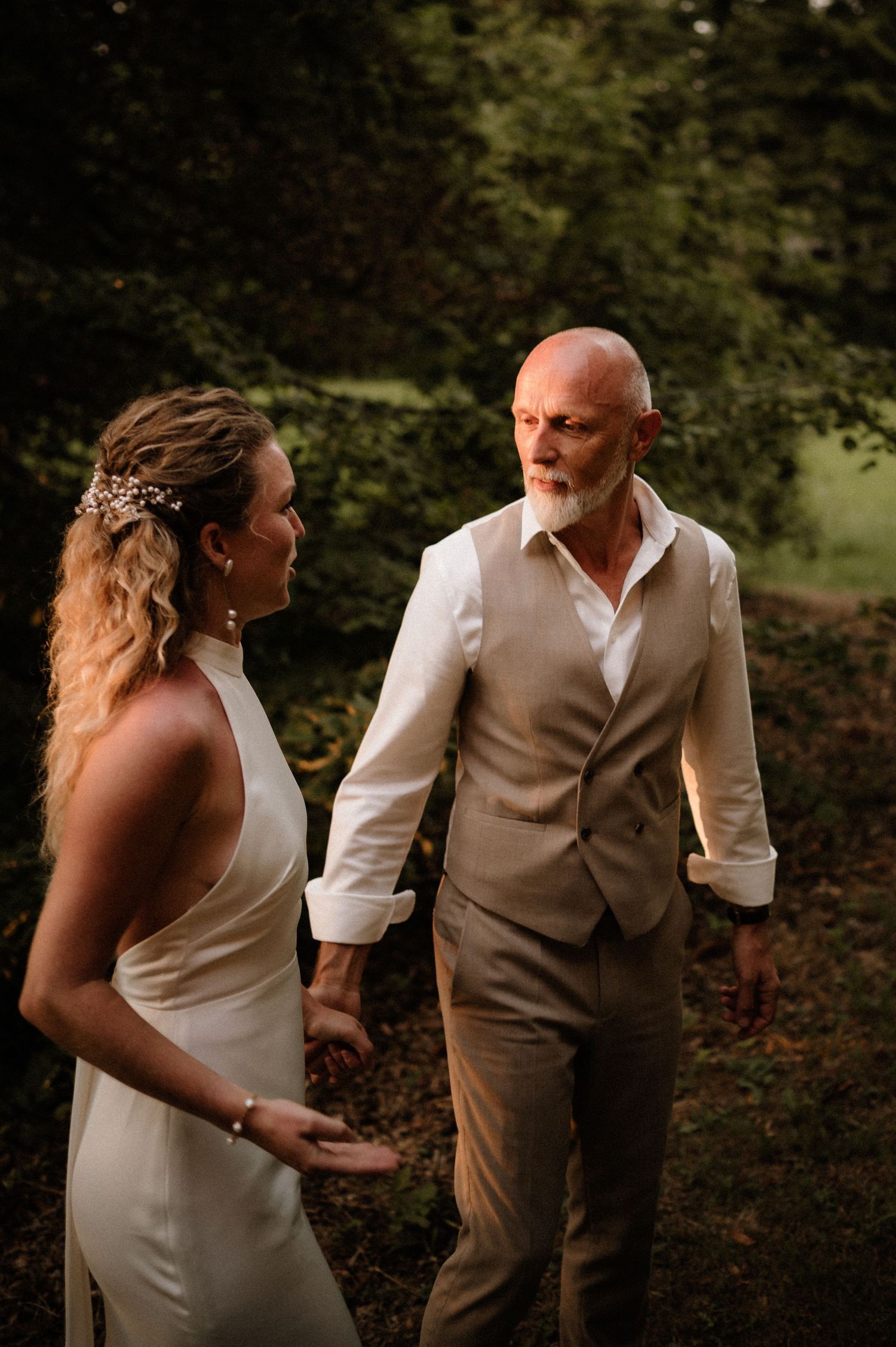 A couple shares an intimate moment in formal attire against a natural backdrop at golden hour.