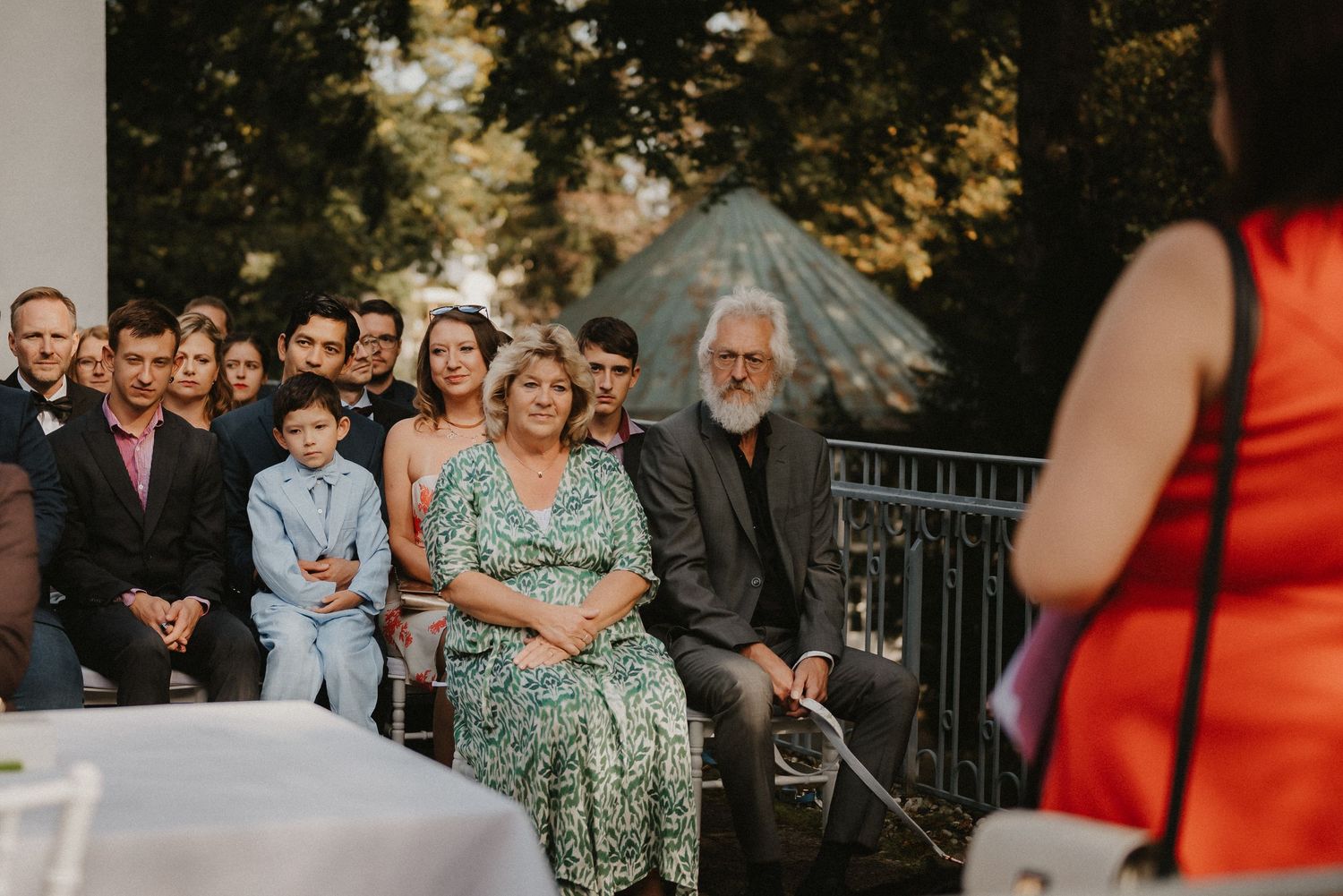 Panoramic view of wedding ceremony guests seated in white chairs at an outdoor venue.