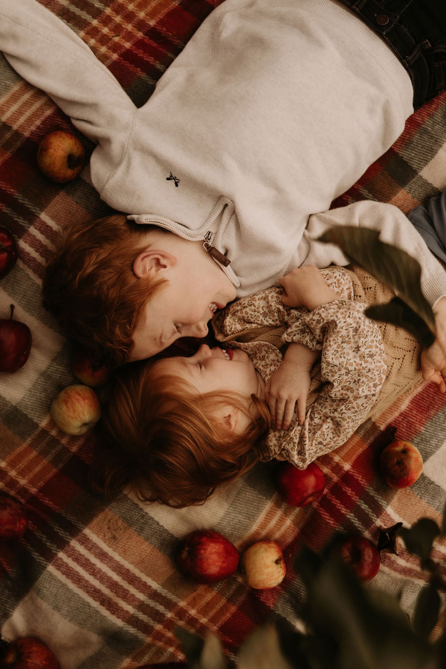 Siblings lying together on a blanket surrounded by apples during a cozy outdoor documentary family photoshoot in an apple orchard
