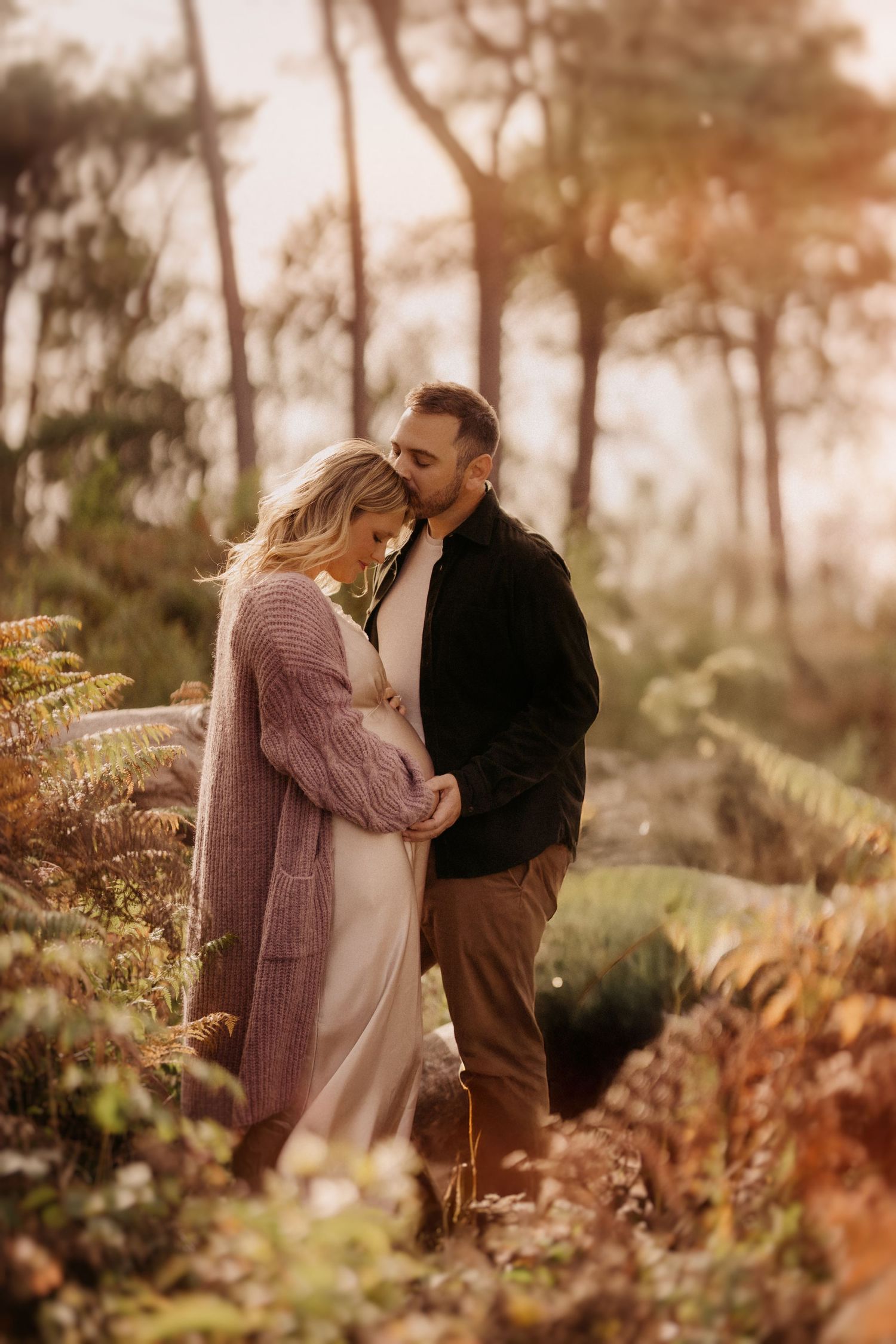 Expecting mother with partner in autumn ferns, captured in soft evening light during a storytelling shoot.