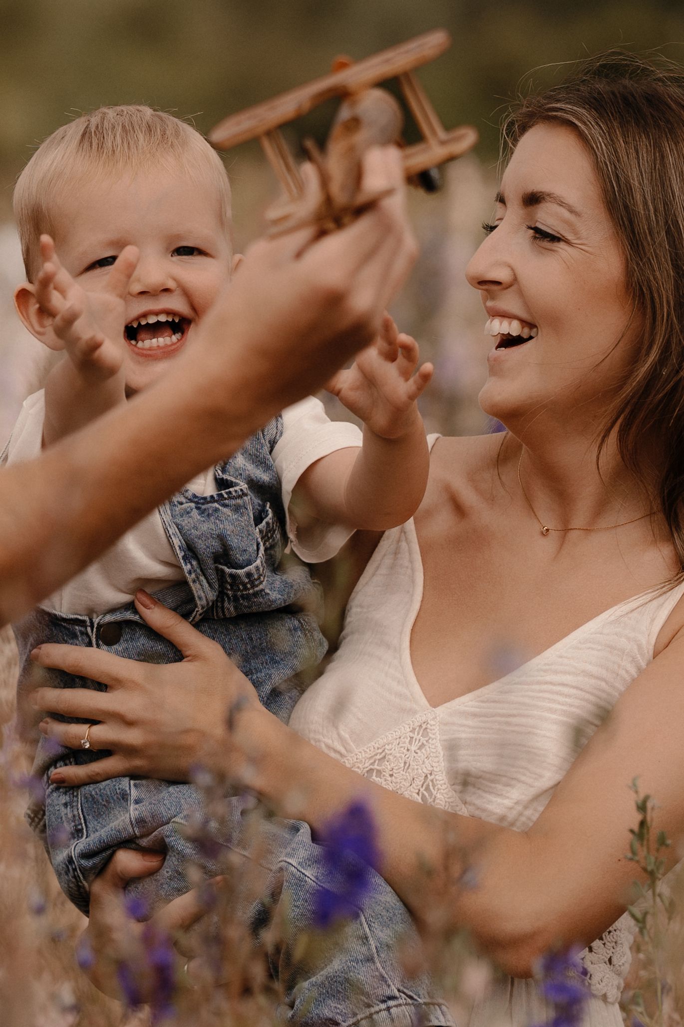 happy hild reaching a wooden airplane with his hands, held by his mum in his arm, taken at Confetti Field