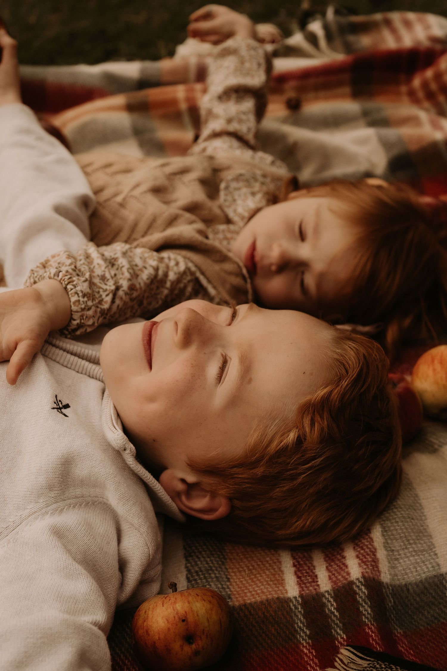 Two siblings nap on a blanket with apples around them during an autumn family storytelling session in Lichfield