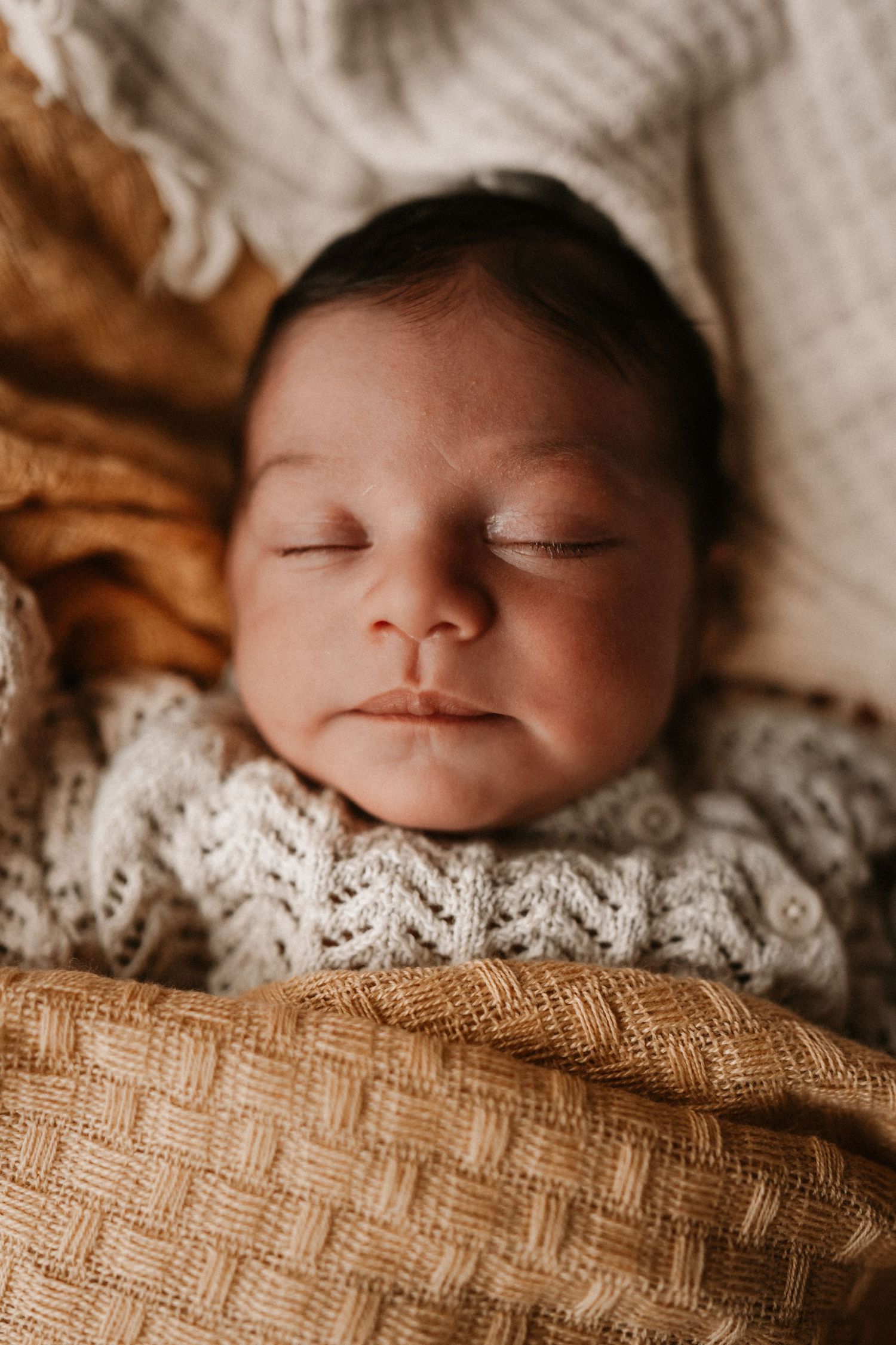 Sleeping newborn wrapped in knit layers during a gentle storytelling newborn photoshoot at home.