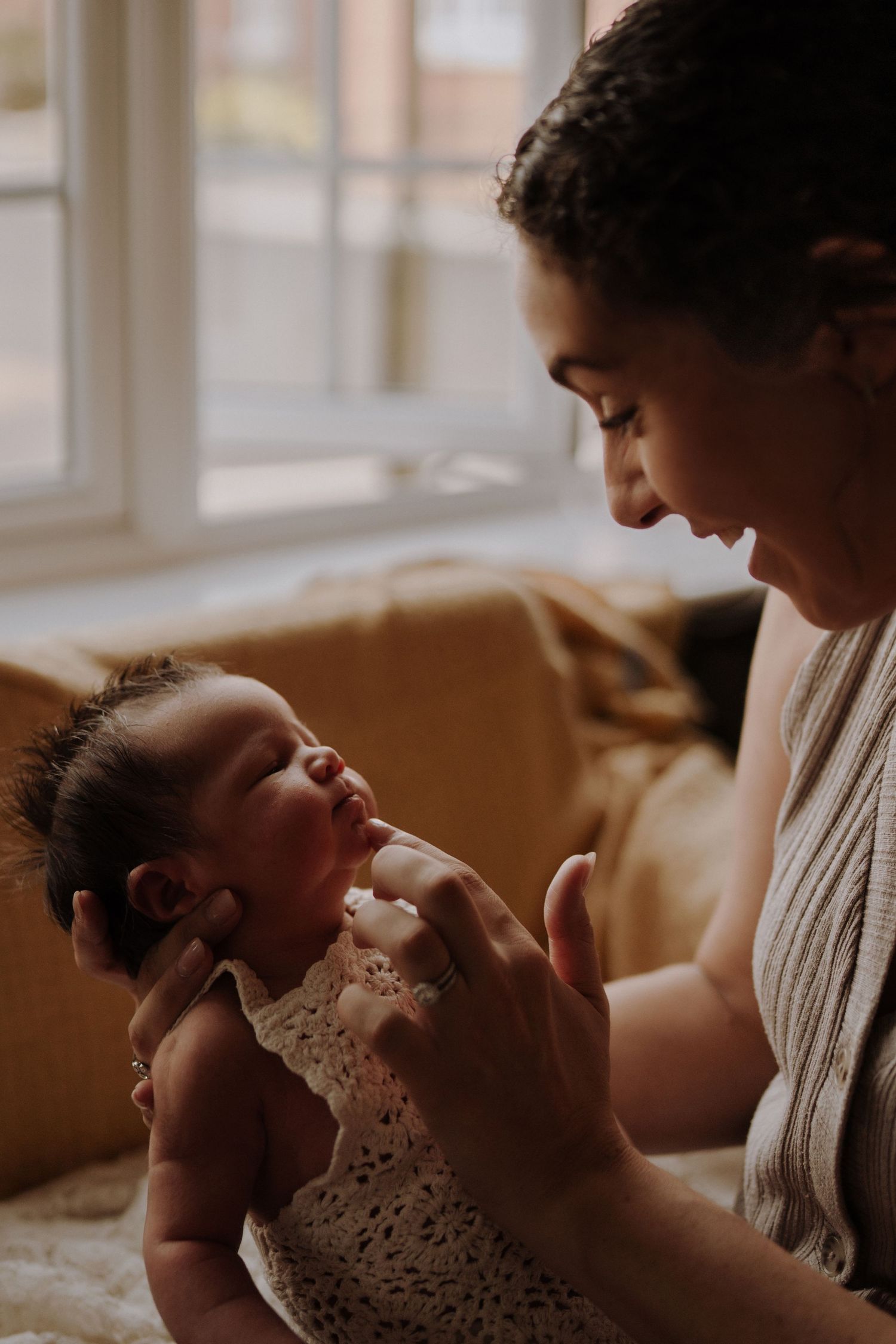 Mother smiles at her newborn by the window, their faces lit with soft natural morning light in Swadlincote