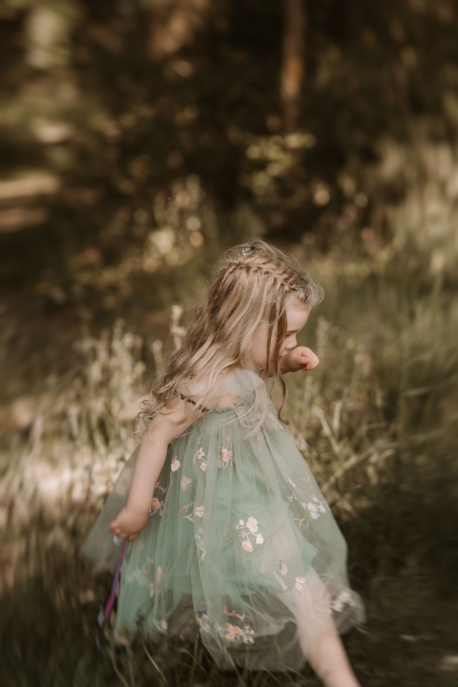 Little girl in a green fairy dress twirls through tall grass during a soft outdoor family session.