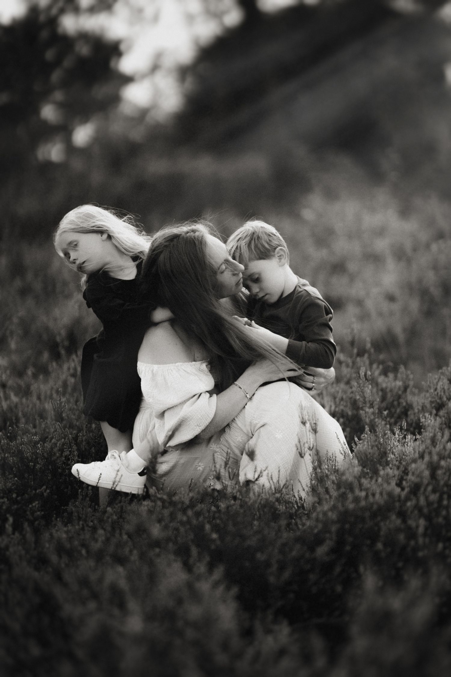 Mum cuddles her daughter and son in tall grass during an emotive family photography session in Birmingham.