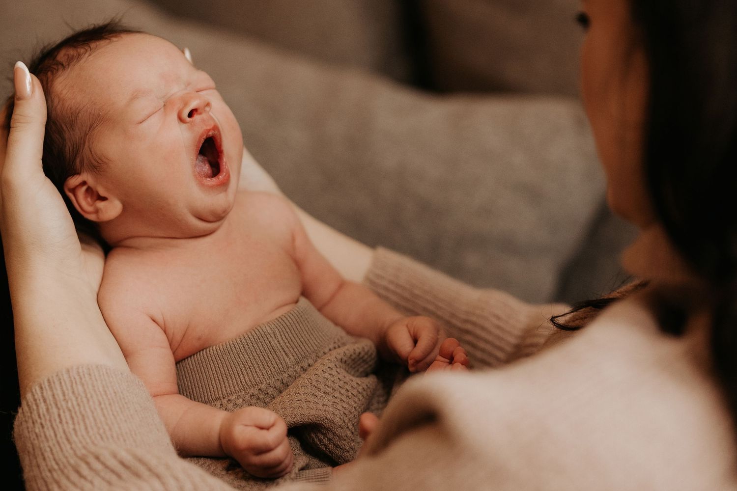 Newborn yawning in a parent’s arms during an in-home natural light lifestyle newborn photography session in Hinckley