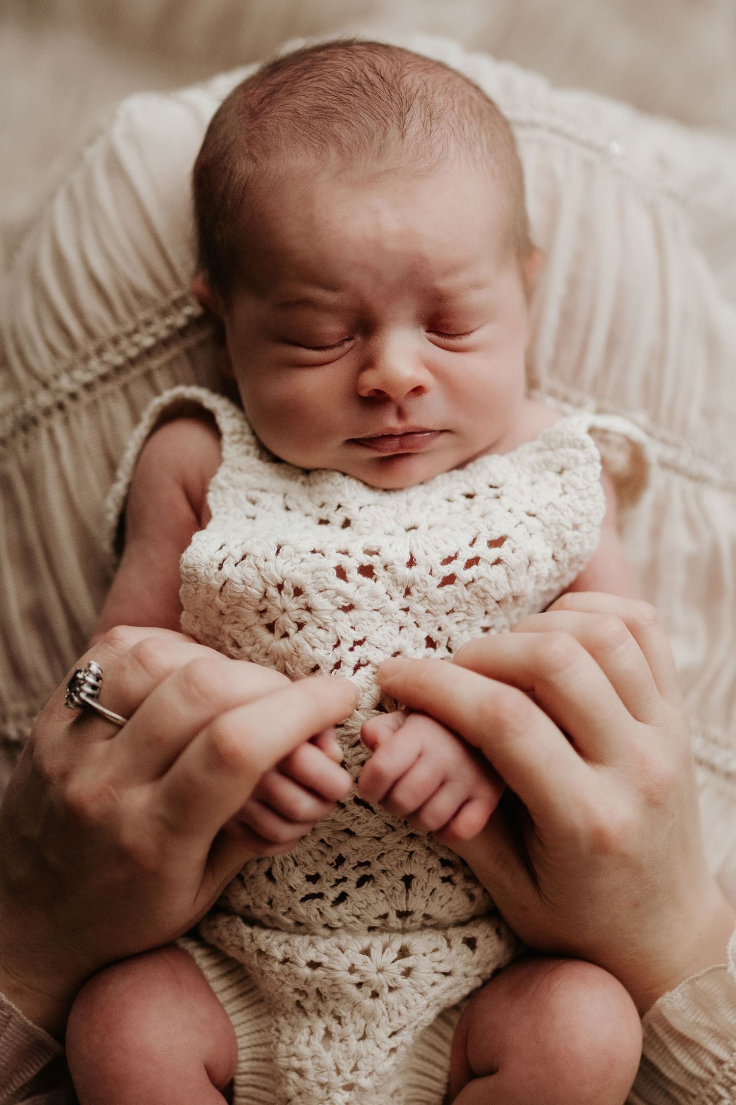Newborn sleeping peacefully while held by gentle hands, documented in a calm, unposed lifestyle photoshoot.