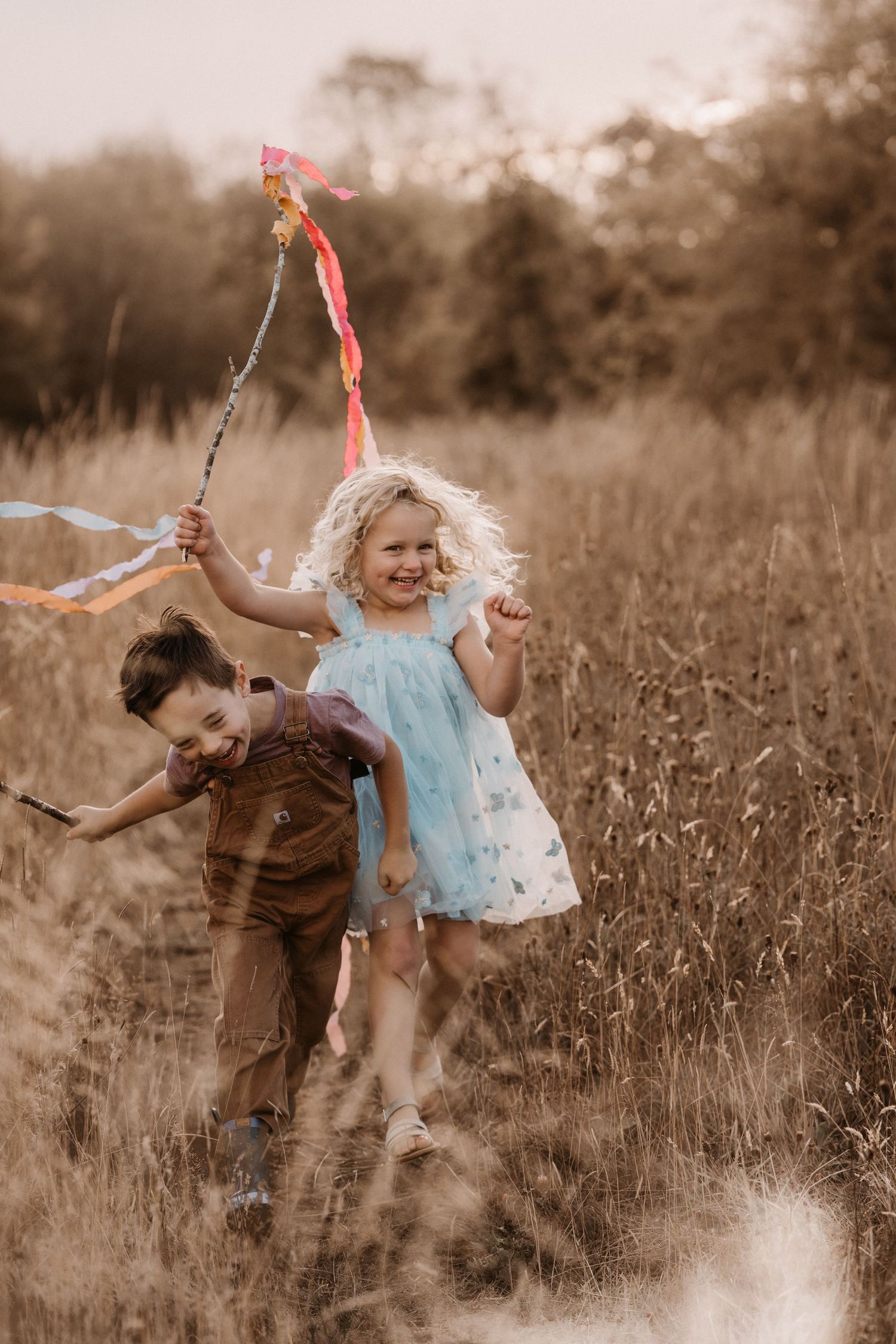 Children running through tall grass with ribbons during a joyful outdoor documentary childhood photoshoot in Moira