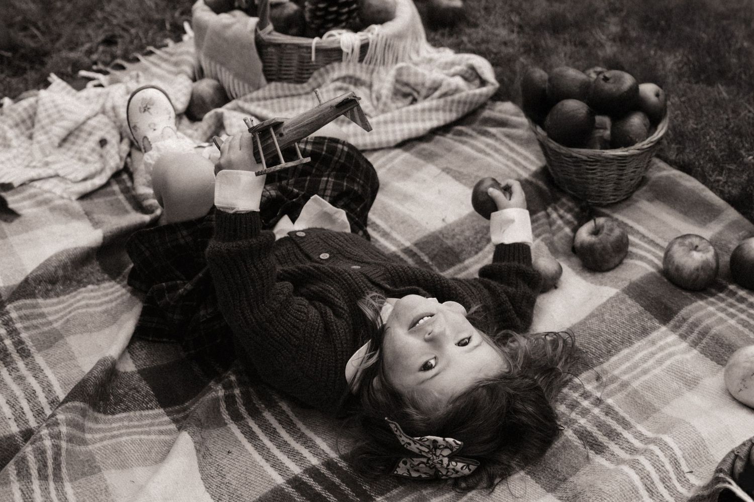 Child lies on a picnic blanket surrounded by apples during an autumn orchard storytelling photoshoot.