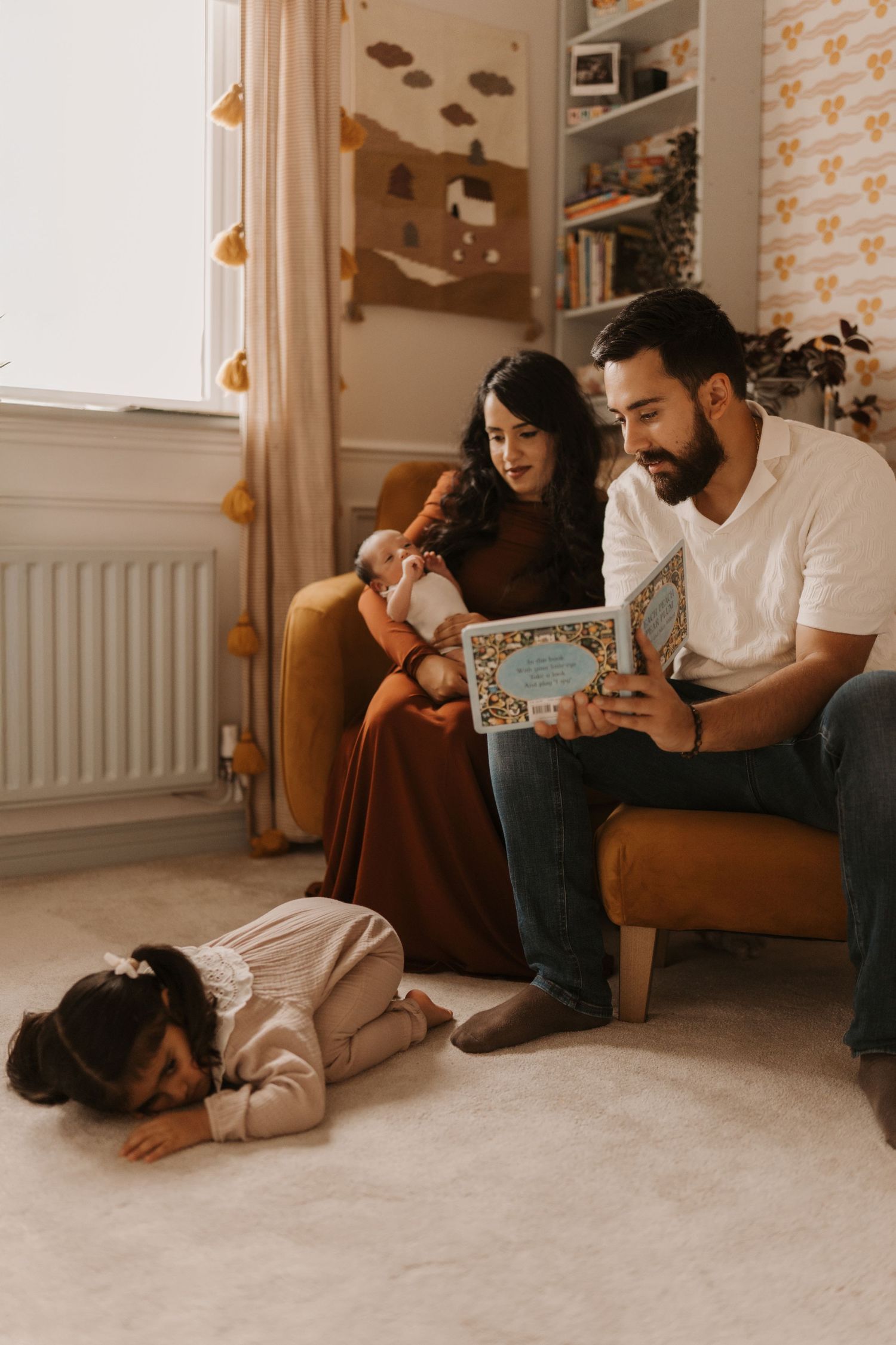 Family reading together at home while a toddler rests nearby during a relaxed lifestyle family photoshoot.