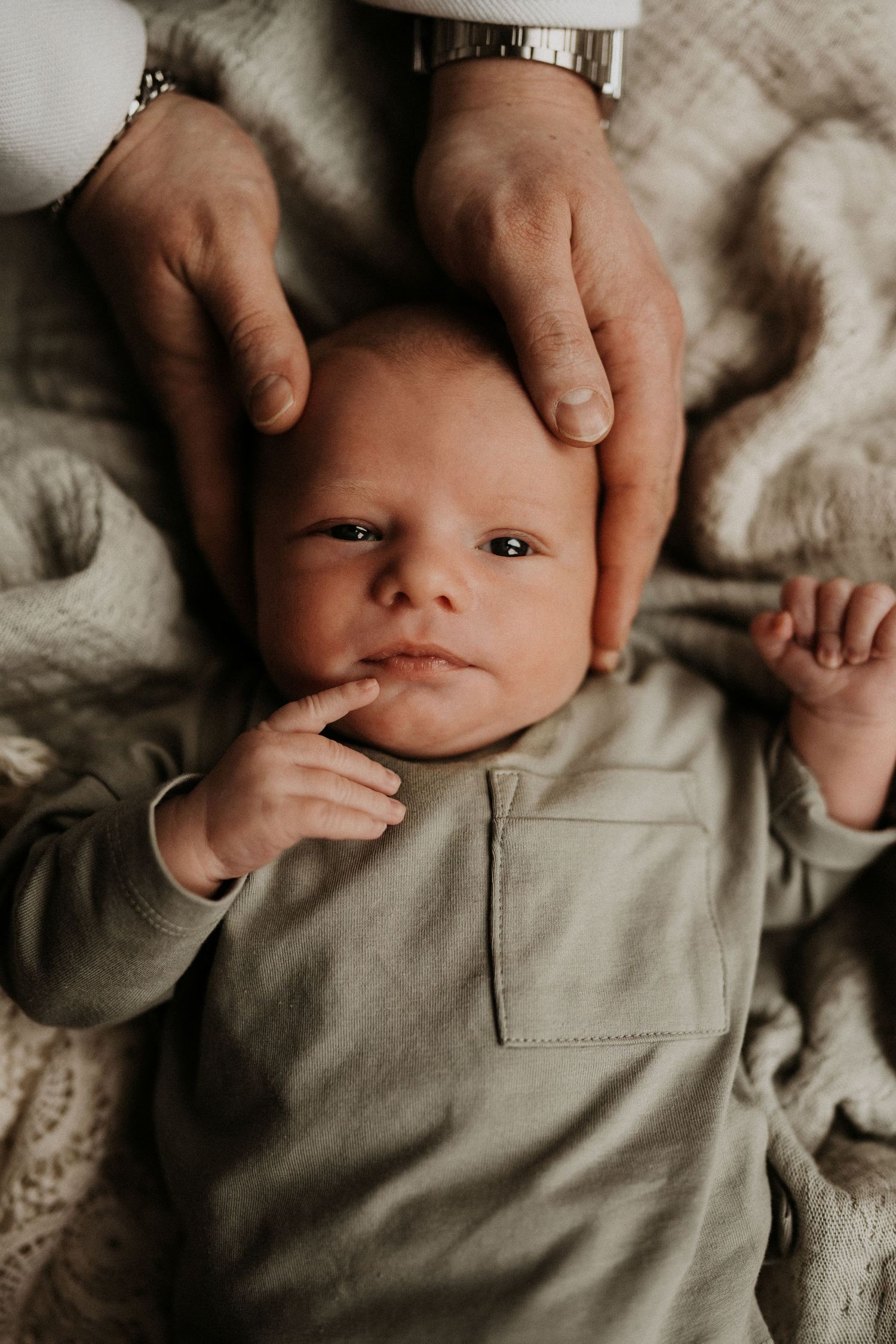 Newborn lying on a bed while parents touch their hands during an in-home lifestyle newborn photography session in Swadlincote