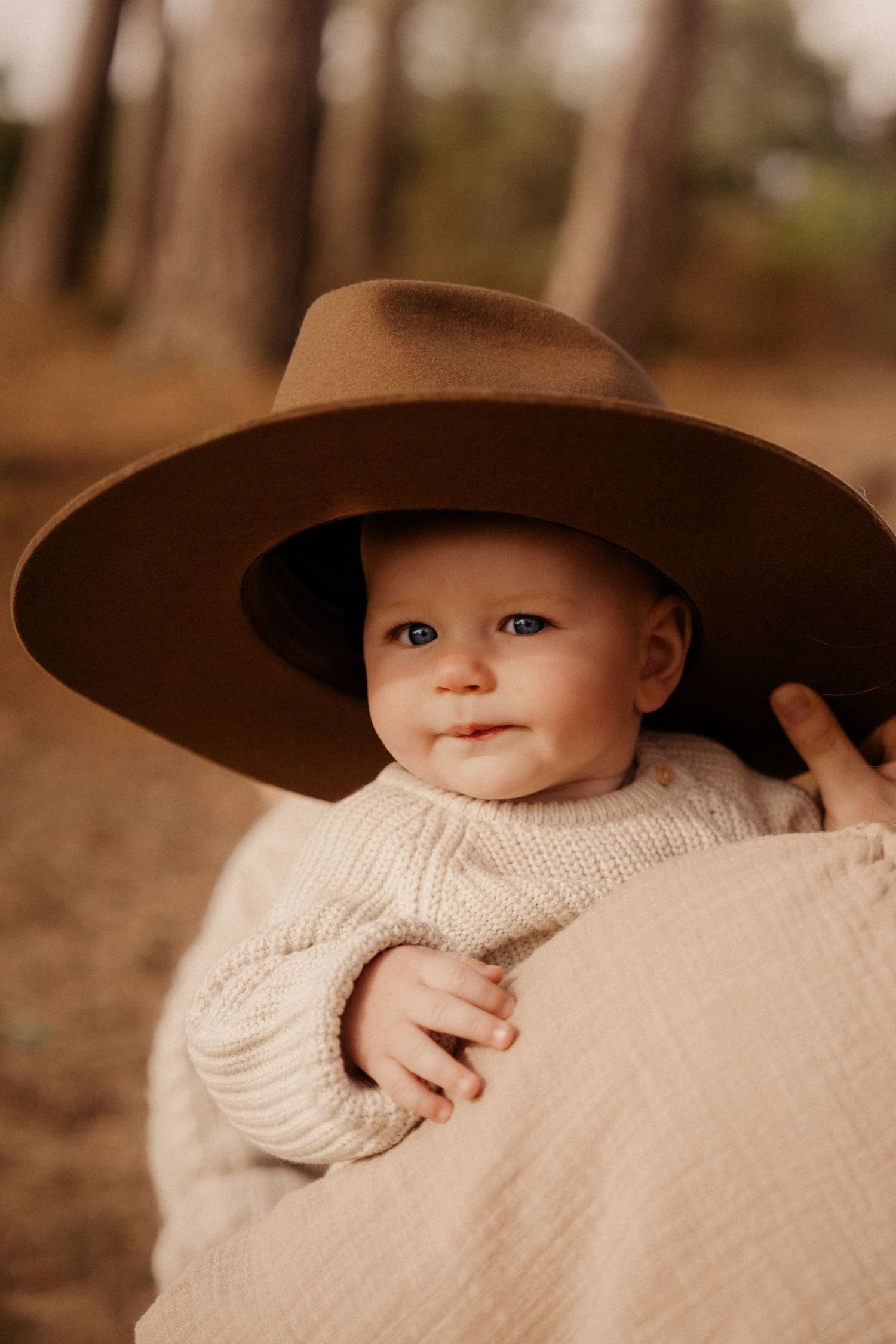 Baby wrapped in a blanket wears a wide hat during a warm autumn family photoshoot outdoors in Birmingam, Lickey Hill