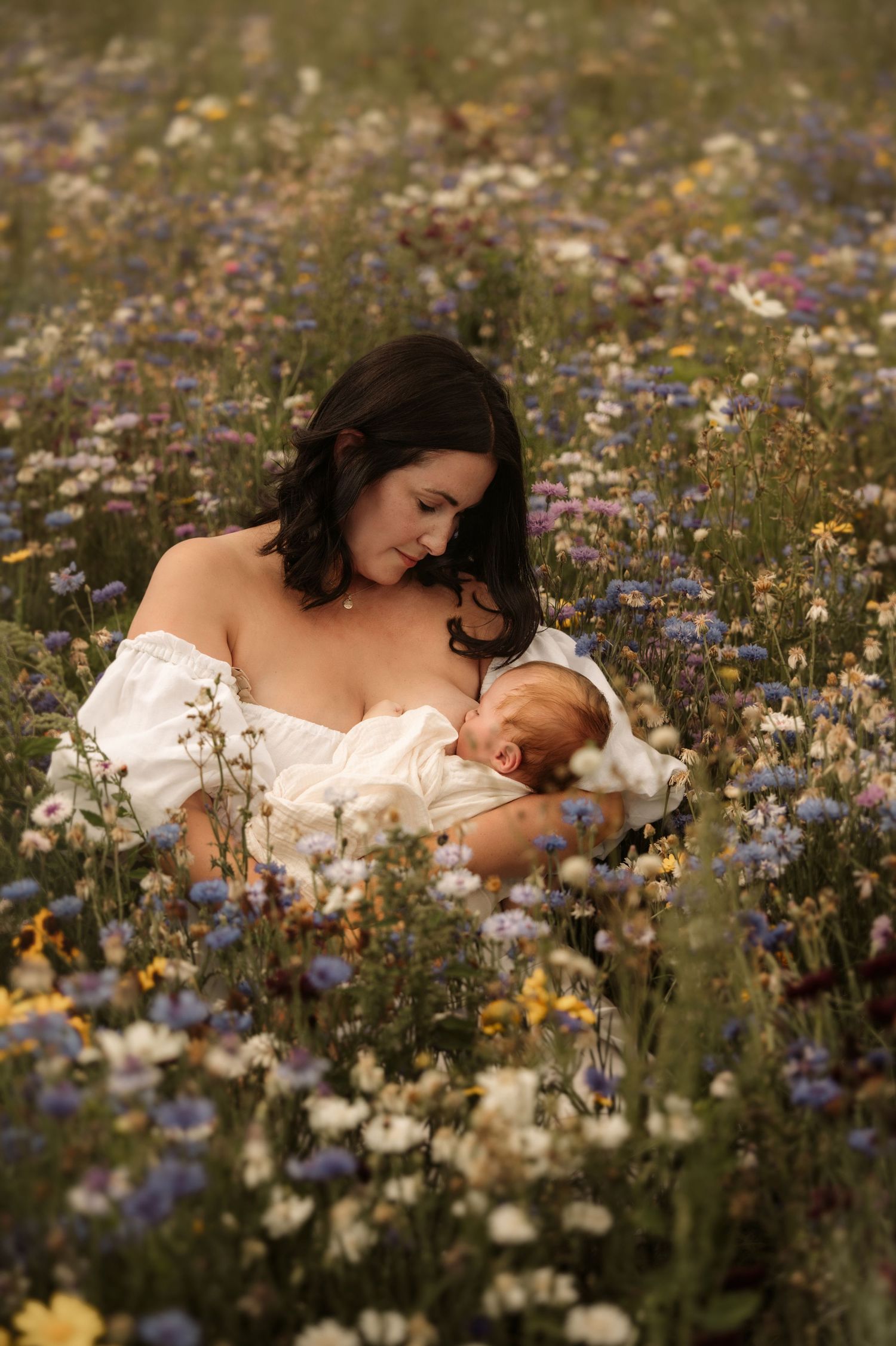 Mother holding her newborn in a wildflower meadow during a calm outdoor documentary motherhood photoshoot.
